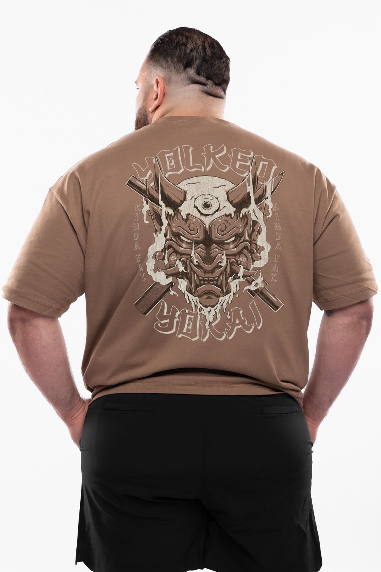 Man wearing a brown t-shirt with a graphic design on the back, standing against a white background