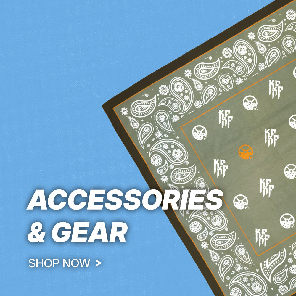 Promotional graphic for accessories and gear, featuring a folded bandana with a white paisley pattern on a muted olive green background, set against a solid blue background with 'ACCESSORIES & GEAR' and 'SHOP NOW >' text.