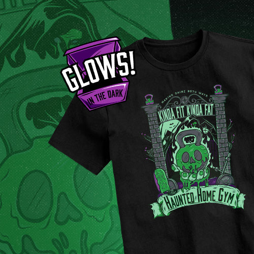 A black short-sleeve graphic T-shirt laid flat on a green patterned background. The shirt features a Halloween-themed graphic with a skull in a nurse outfit, brick archway, and text reading 'KINDA FIT KINDA FAT' and 'HAUNTED HOME GYM.